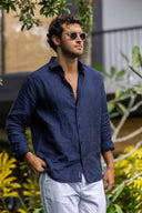 Man in navy shirt and white pants standing in a garden with yellow flowers and greenery.